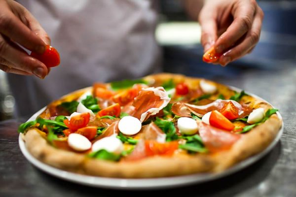 Foto de um homem preparando pizza, com foco nas mãos do pizzaiolo e no produto
