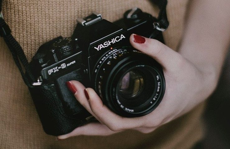 Para ilustrar os cursos da Rede Cuca, uma mão feminina com unhas pintadas de vermelho segura uma câmera analógica da marca Yashica