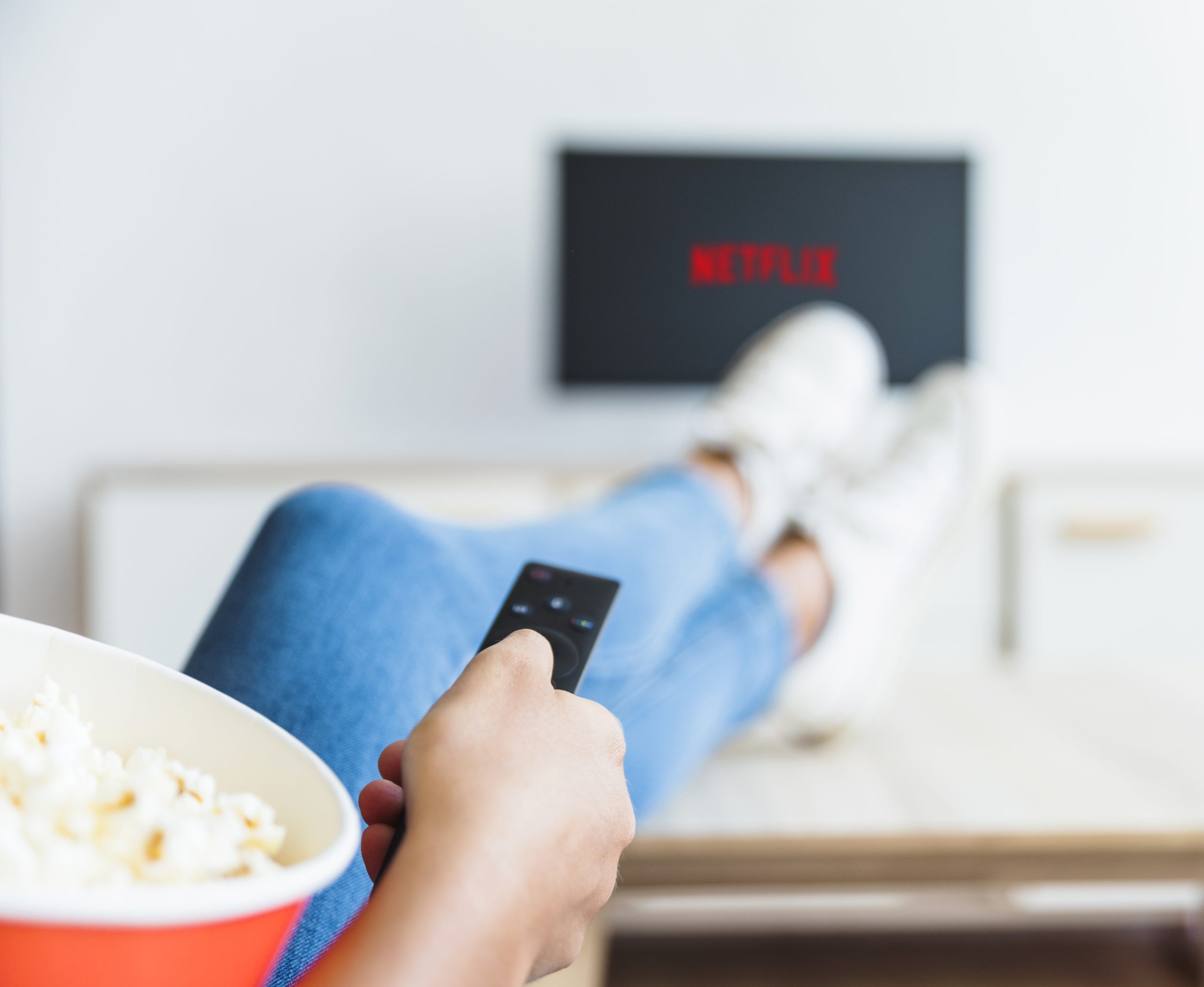 Pessoa com controle na mão apontando para TV com logo da Netflix; POP Empregos&Carreiras selecionou três série da Netflix
