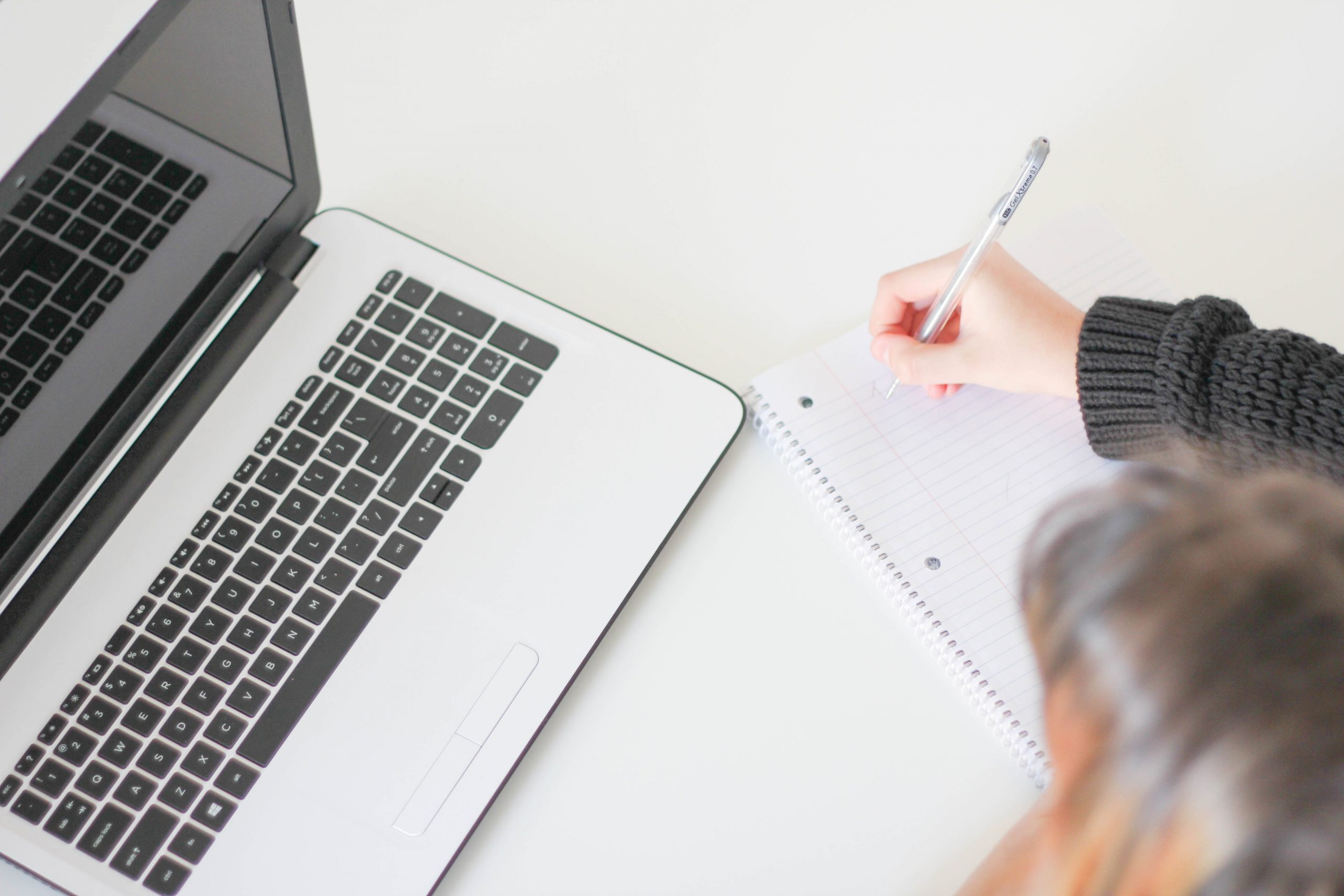 Mulher em frente a um notebook, com caneta e papel na mão; Saber Virtual é plataforma online para quem quer capacitar-se