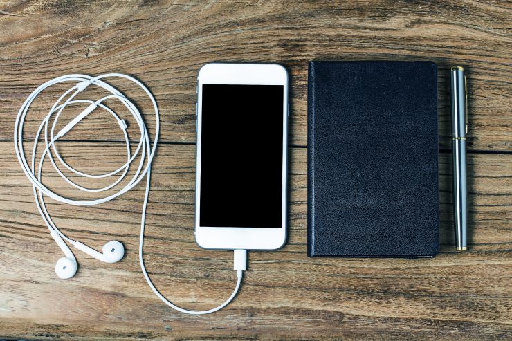 Smartphone com fone de ouvidos e caderneta; podcasts de empreendedorismo são opção para quarentena