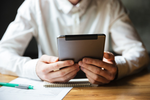 Homem segurando tablet com caneta e caderno; conheça as leis no home office