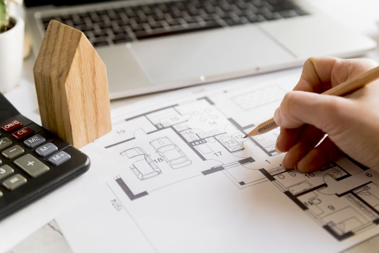 Mão desenhando projeto arquitetônico perto de um notebook; ArchaPLAY é voltada a profissionais de arquitetura e design de interiores