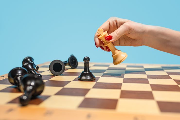 Mão feminina mexendo peça em tabuleiro de xadrez, simulando tomada de decisão e uso da inteligência emocional