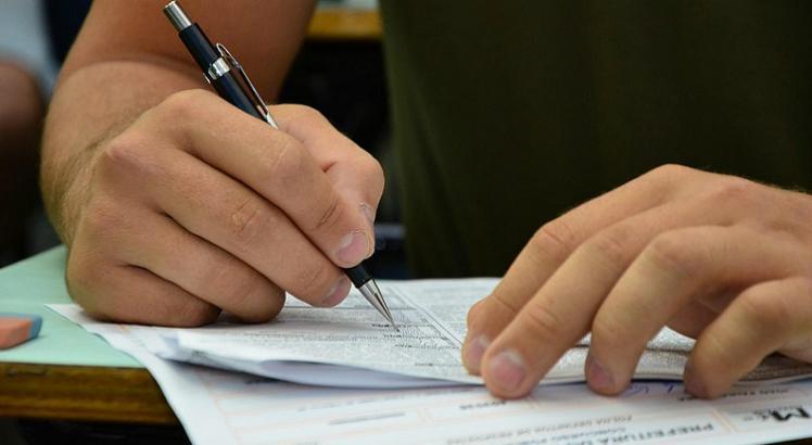 Concursos: pessoa escrevendo com caneta em uma prova 