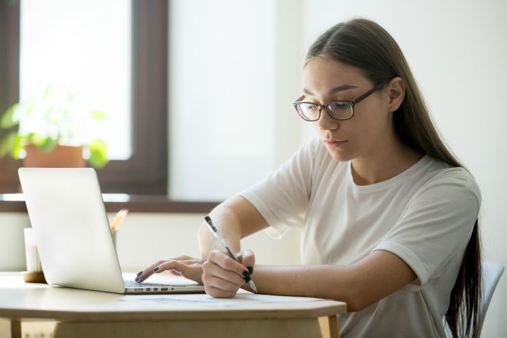 Mulher digitando em notebook e tomando no em papel; maratona de aula prepara concurseiros