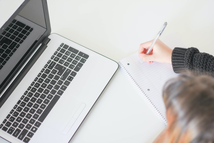 Concursos no Nordeste: confira sete oportunidades para 2020. Na foto, uma mulher faz anotações em um bloco de notas branco em frente a um notebook de cor grafite.