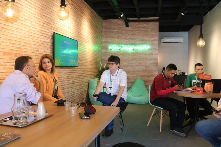 Consultoria: na imagem, a recepção do campus Aldeota, com mesa, cadeiras verdes e pessoas conversando ao redor de uma mesa de madeira.