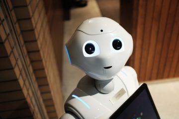 Robôs: na imagem, um robô branco olha para a câmera. Ele possui olhos e boca pretos e aparenta segurar um tablet preto.